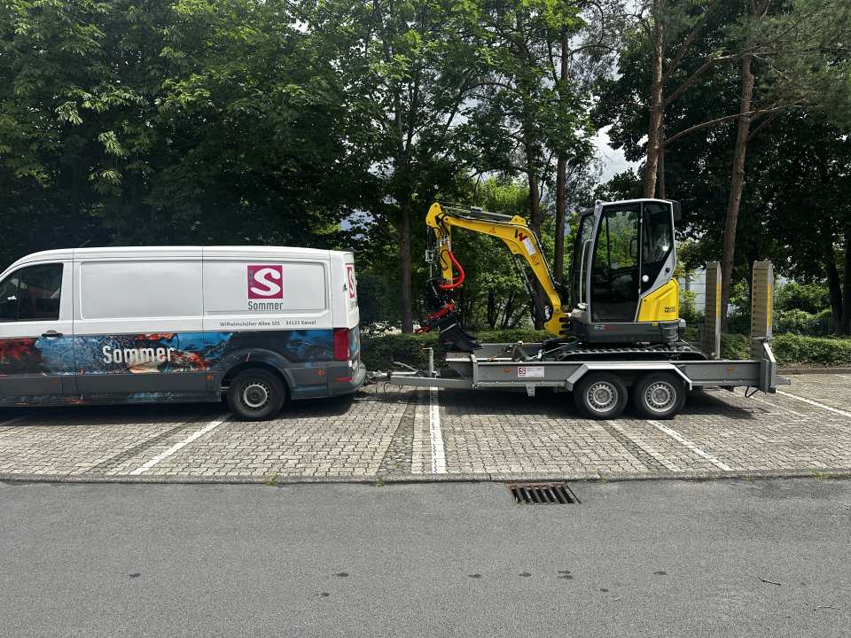 Sommer-Service-Fahrzeug mit gelbem Minibagger auf einem Anhänger an einer Baustelle