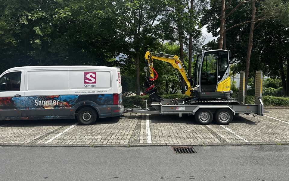 Sommer-Service-Fahrzeug mit gelbem Minibagger auf einem Anhänger an einer Baustelle
