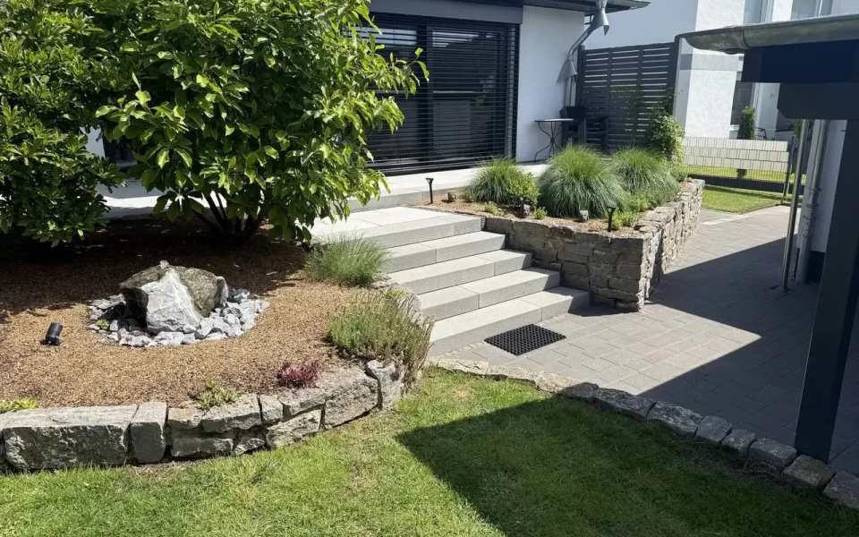Gepflegte Gartenanlage mit Natursteinbeeten, breiter heller Treppenanlage und gepflastertem Zugang